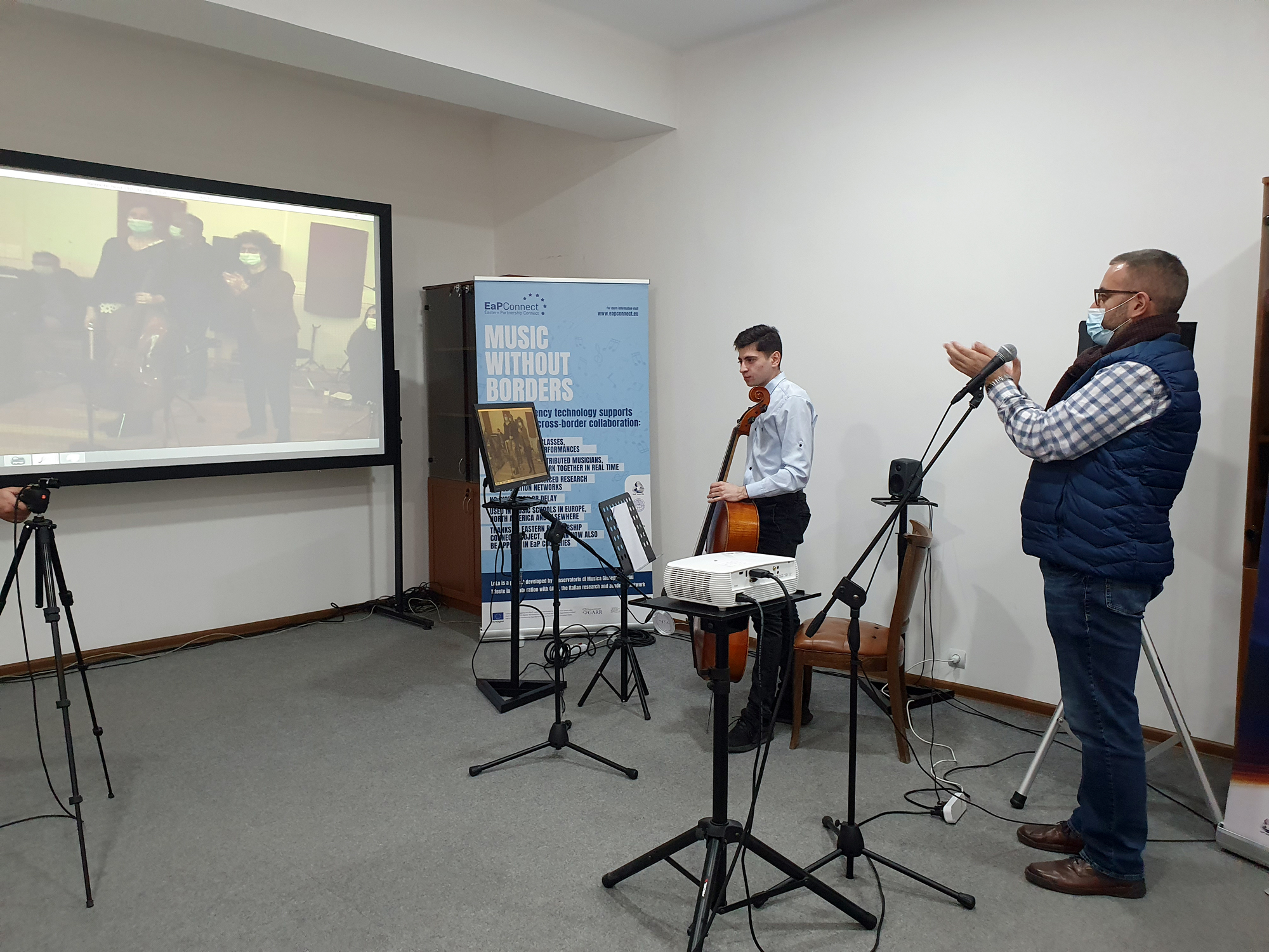 man applauding cellist and people on a screen